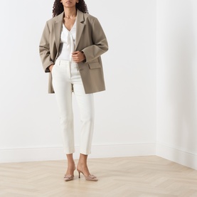 Model wearing Marella white slim-fit trousers styled with a taupe oversized blazer and white top, nude heels.