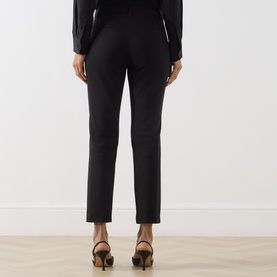 Model wearing Marella black slim-leg trousers, rear view, styled with a black top and black heeled sandals.