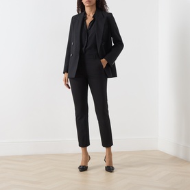 Model wearing Marella black slim-leg trousers, styled with a matching black blazer, shirt, and flat pointed-toe shoes.