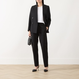Model wearing Marella black tailored trousers with matching black blazer, white top, and black heels. Small black bag held in hand.