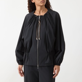Model wearing Max&Co Moli Technical Blouse in black with drawstring neckline, two-way zip, and elasticated waist, styled with black trousers.