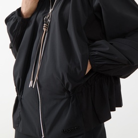 Model wearing Max&Co Moli Technical Blouse in black, showing two-way zip fastening, oversized zip pull and elasticated drawstring detail at neckline.