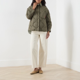 Model wearing olive green quilted jacket with onion stitch pattern, styled with cream wide-leg trousers and tan mules