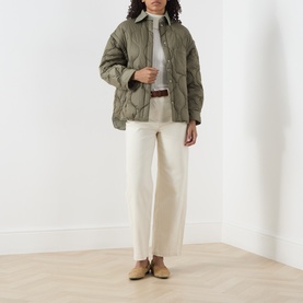Model wearing khaki quilted jacket with diamond pattern, styled with white trousers, grey turtleneck, brown belt and tan loafers