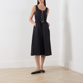 Model wearing Max&Co black sleeveless midi dress with zip front detail and belted waist, styled with black flat mules