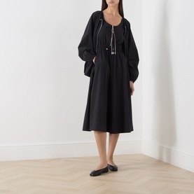Model wearing Max&Co black midi dress with balloon sleeves, gathered waist, tassel tie neckline, styled with black flat shoes.