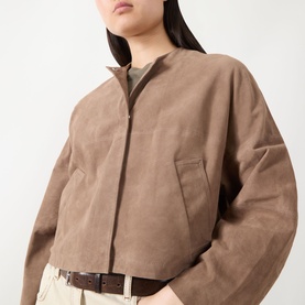 Model wearing Max&Co turtledove goat leather zip-up jacket with chest pocket, styled with beige trousers and brown belt.