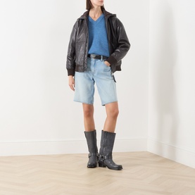 Model wearing Max&Co dark brown leather jacket with blue denim shorts, styled with a blue knit top and black harness boots.