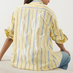 Model wearing Max&Co Dama Stripe Shirt in yellow with blue stripes and white slogan graphic on back, styled with light blue jeans.