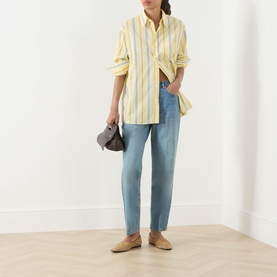 Model wearing Max&Co Dama Stripe Shirt in yellow with blue stripes, styled with light blue jeans, taupe loafers, and carrying a small brown bag.