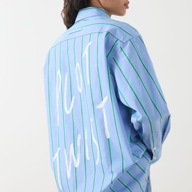 Model wearing Max&Co Dama Stripe Shirt in light blue with green stripes and white slogan graphic to the back, long sleeves, dropped shoulders