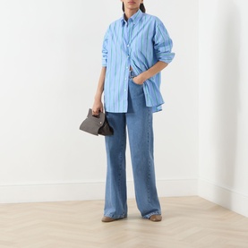 Model wearing Max&Co Dama Stripe Shirt in light blue cotton, styled with wide-leg jeans and carrying a small brown bag.