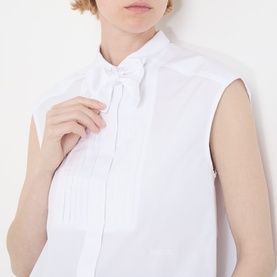 Model wearing Max&Co optical white sleeveless cotton shirt with tie neck bow detail, front pleat panel visible at close crop