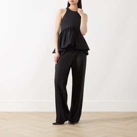 Model wearing Max&Co Pietre Peplum Top in black satin with balloon peplum hem, styled with wide-leg black trousers.