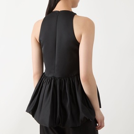 Model wearing Max&Co Pietre Peplum Top in black, showing rear zip, sleeveless silhouette and gathered balloon peplum hem in satin fabric.