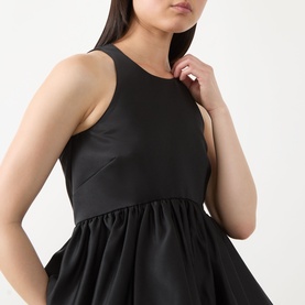 Model wearing Max&Co Pietre Peplum Top in black satin, round neckline, sleeveless, with gathered balloon-hem peplum detail.