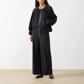 Model wearing Max&Co Orche Black Technical Straight Leg Trousers with a black zip-up jacket and flat loafers.
