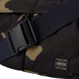 Porter Yoshida bag in Woodland Khaki camouflage, close-up of black buckle clasp and navy webbing strap with branded label