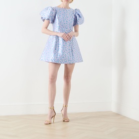 Model wearing Sister Jane Wisteria Jacquard Mini Dress in blue floral jacquard with puff sleeves and voluminous skirt, styled with gold strappy heels