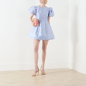 Model wearing Sister Jane Wisteria Jacquard Mini Dress in blue floral, with puff sleeves and voluminous skirt, styled with nude heels and pink clutch.
