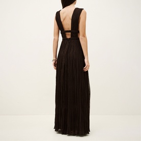 Model wearing Bash Tania Pleated Dress in brown, showing open back with cut-out waist detail and floor-length pleated skirt.