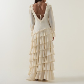 Model wearing Anne Louise Boutique Cream Dress, back view showing open tie neckline, long sleeves, and tiered ruffle maxi skirt.
