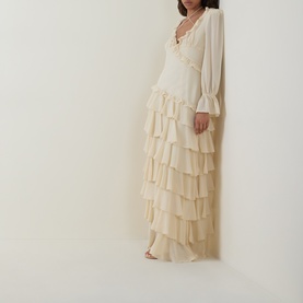 Model wearing Anne Louise Boutique cream maxi dress with tiered ruffle skirt, V-neckline with lace trim, and long billowy sleeves