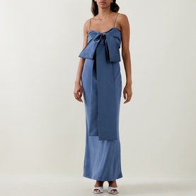 Model wearing Bernadette mid blue maxi dress with oversized front bow detail and thin straps, styled with white strappy heels.