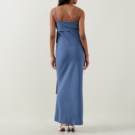 Model wearing Bernadette mid blue satin maxi dress, back view, featuring thin straps and oversized black bow detail at waist.