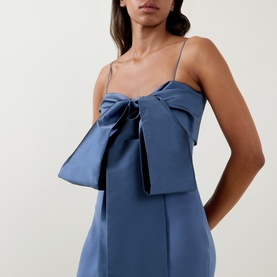 Model wearing Bernadette mid blue satin slip dress with oversized front bow detail and thin shoulder straps, close-up crop view.