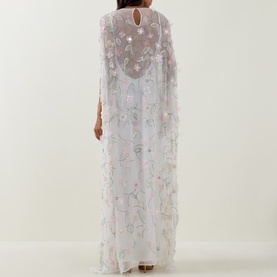 Model wearing Bernadette dress in Clematis Emb White, sheer floral embroidered cape overlay, back view, floor-length silhouette