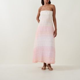 Model wearing Bernadette strapless maxi dress in Spanish Seaside ombre pink-to-white, with gold flat sandals.
