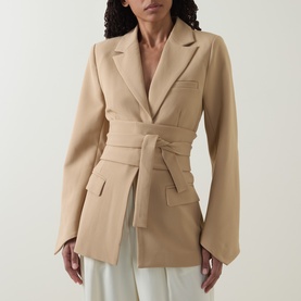 Model wearing Odd Muse camel blazer top with tie waist belt, styled with white wide-leg trousers.