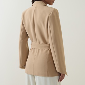 Model wearing Odd Muse camel belted blazer, back view, paired with white wide-leg trousers