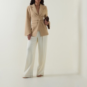 Model wearing Odd Muse camel belted blazer top with cream wide-leg trousers, carrying a brown clutch bag.