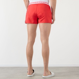 Model wearing Versace vintage red swim shorts, rear view, with white logo waistband and black side stripe detail