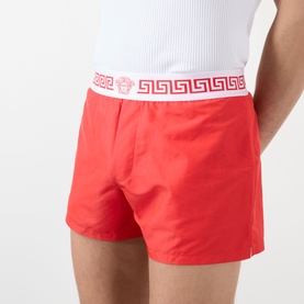 Model wearing Versace vintage red swim shorts with white Greca-border elasticated waistband, styled with white vest top.