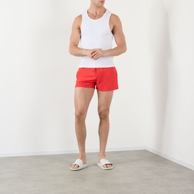 Model wearing Versace vintage red swim shorts, styled with a white vest and white slides.