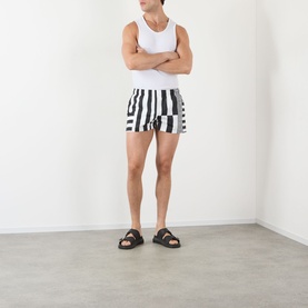 Model wearing Versace black and white geometric stripe swim shorts, styled with a white vest and black slider sandals.