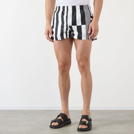 Model wearing Versace black and white stripe and checkerboard swim shorts, styled with black chunky strap sandals.