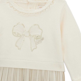 Close-up of cream knit top with gold sequin bow embroidery and lace neckline trim, layered over a pleated skirt