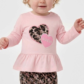 Model wearing Guess 2 Piece set in Polly Pink; long-sleeve peplum top with heart logo print and matching patterned leggings.