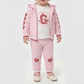 Model wearing Guess Polly Pink 2-piece set with zip-up hoodie and joggers, styled with white graphic tee and pink shoes.