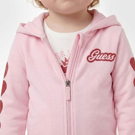 Model wearing Guess Polly Pink zip-up hoodie with logo and heart detail, styled with white printed top underneath.