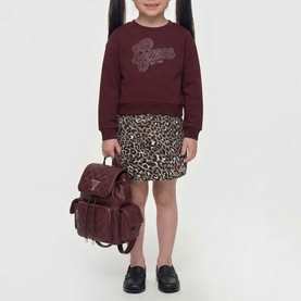 Model carrying Guess children's deep maroon backpack with bow detail; styled with burgundy sweatshirt and leopard print skirt.