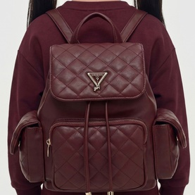 Model carrying Guess deep maroon quilted backpack with gold-tone triangle logo, front zip pockets and drawstring closure