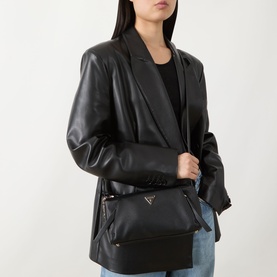 Model carrying Guess Devon Mini Crossbody Bag in black with gold-tone hardware and triangular logo badge, styled with black leather blazer