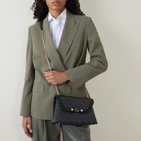 Model carrying black quilted crossbody bag with gold-tone chain strap and logo clasp, styled with sage green blazer and trousers