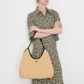 Model carrying Guess Kirsten Woven Hobo Shoulder Bag in natural, black contrast trim, gold triangle logo hardware, styled with a floral midi dress.