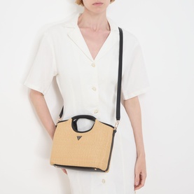 Model carrying a straw and black structured top-handle bag with gold-tone logo detail and black crossbody strap, styled with a white dress.